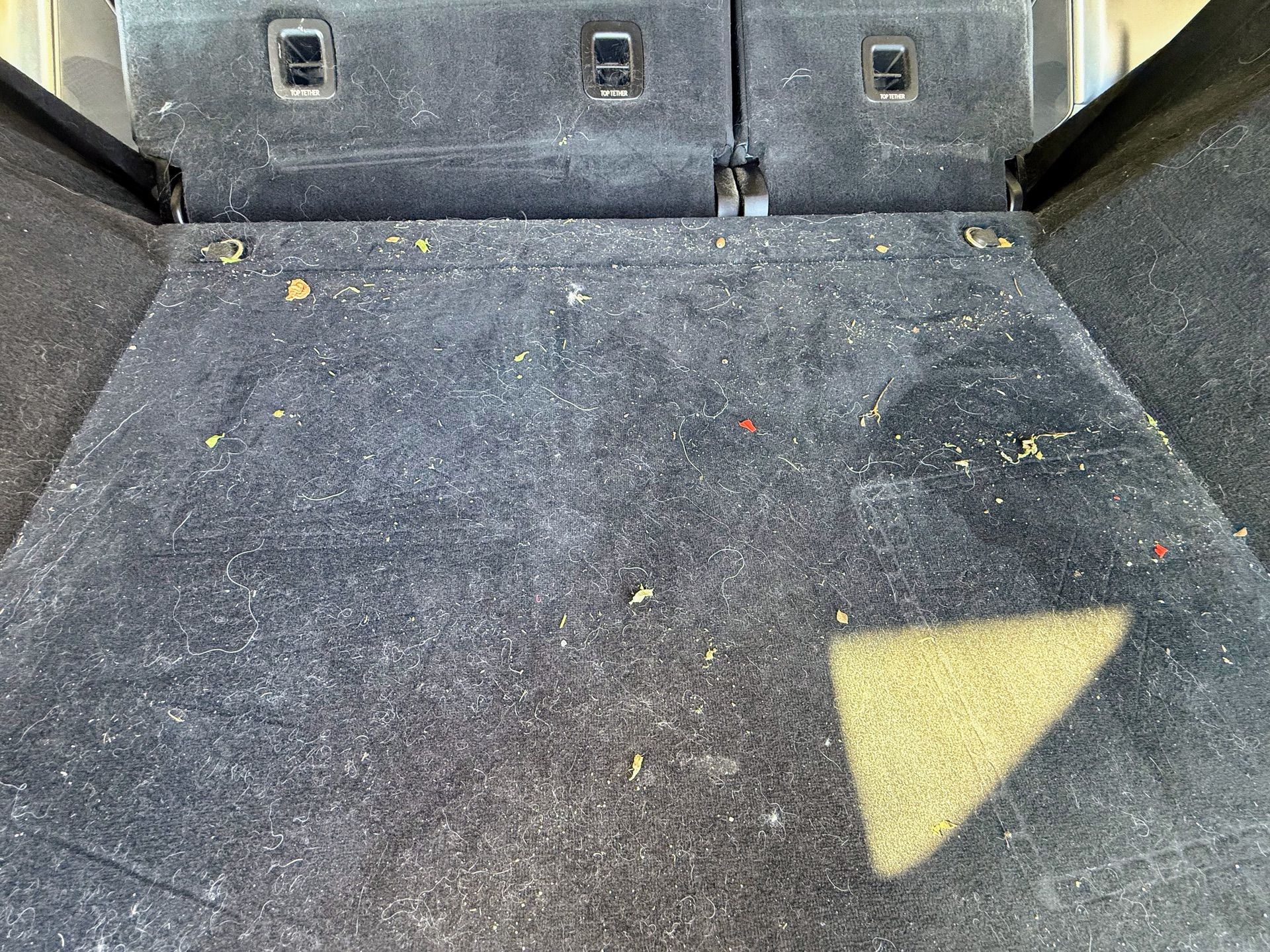 Black car back seat with floor mats, showing texture and some debris.