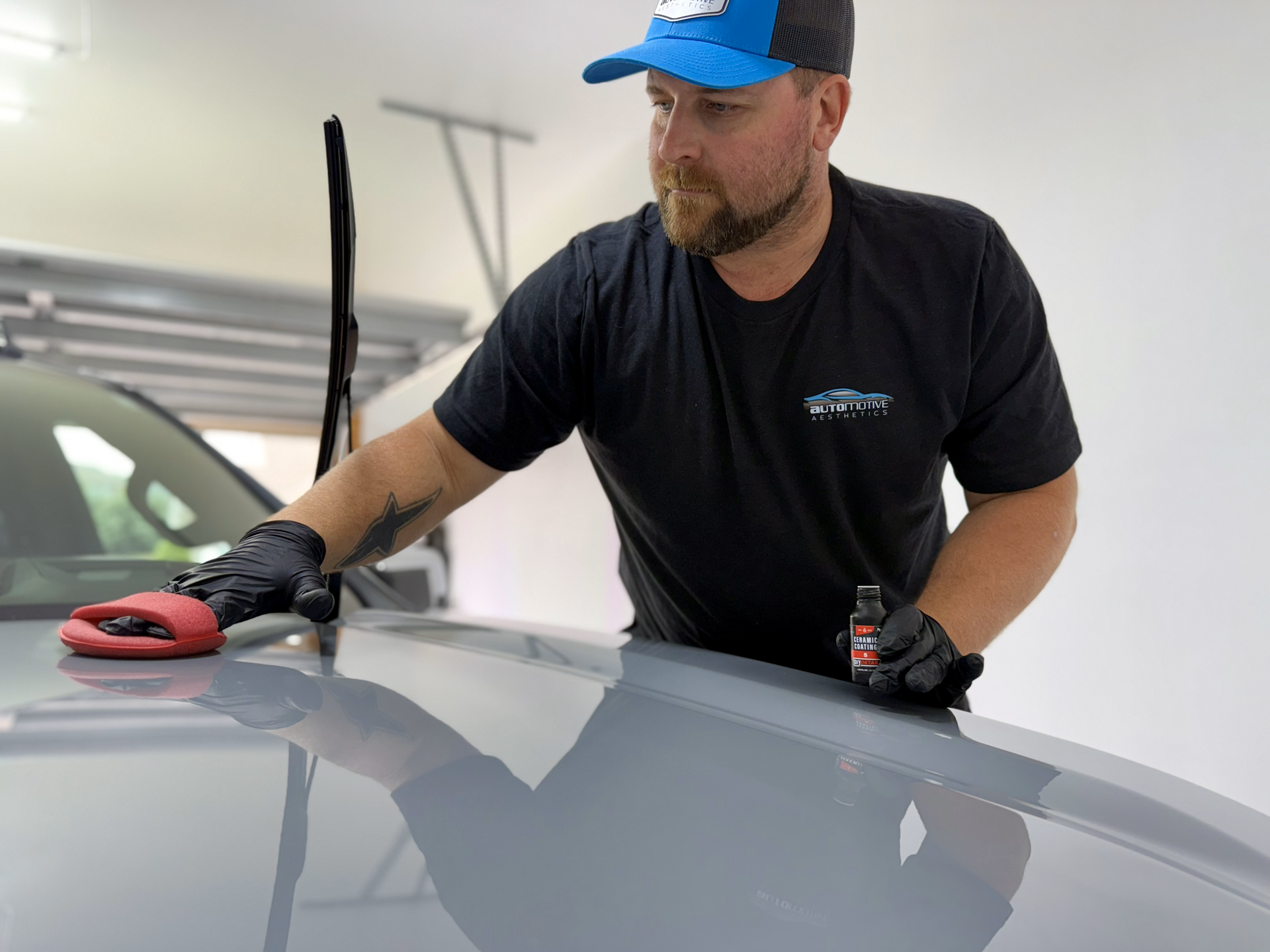 a person wearing black gloves is polishing the hood of a car .