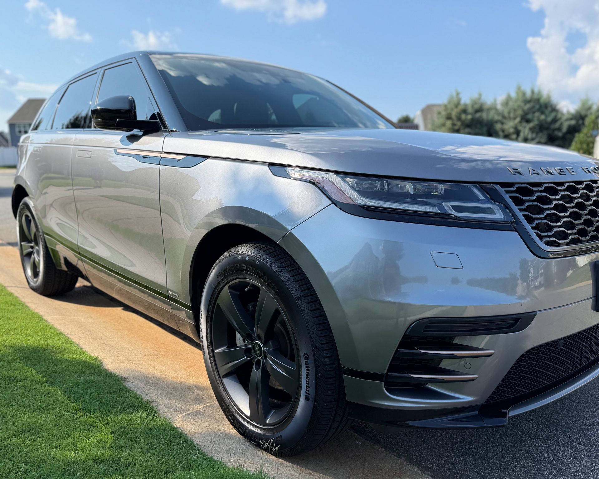 Silver Range Rover Velar parked on a driveway in front of a green lawn on a sunny day.