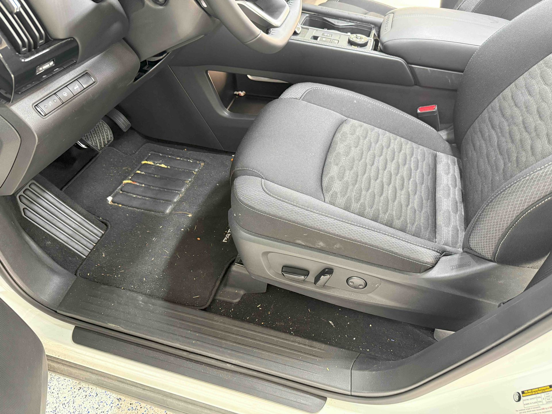 Interior of a car showing the driver's seat, floor mats, and dashboard with debris.