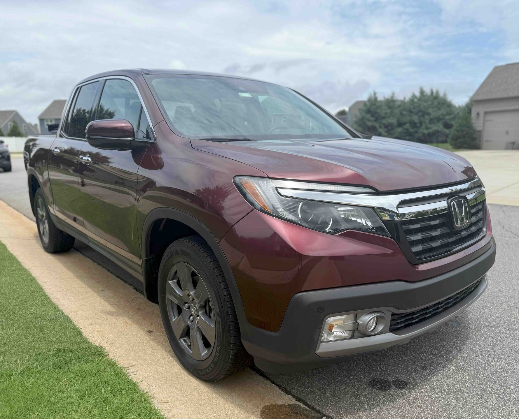 Burgundy Honda Ridgeline pickup truck parked on a street curb with a grassy lawn.