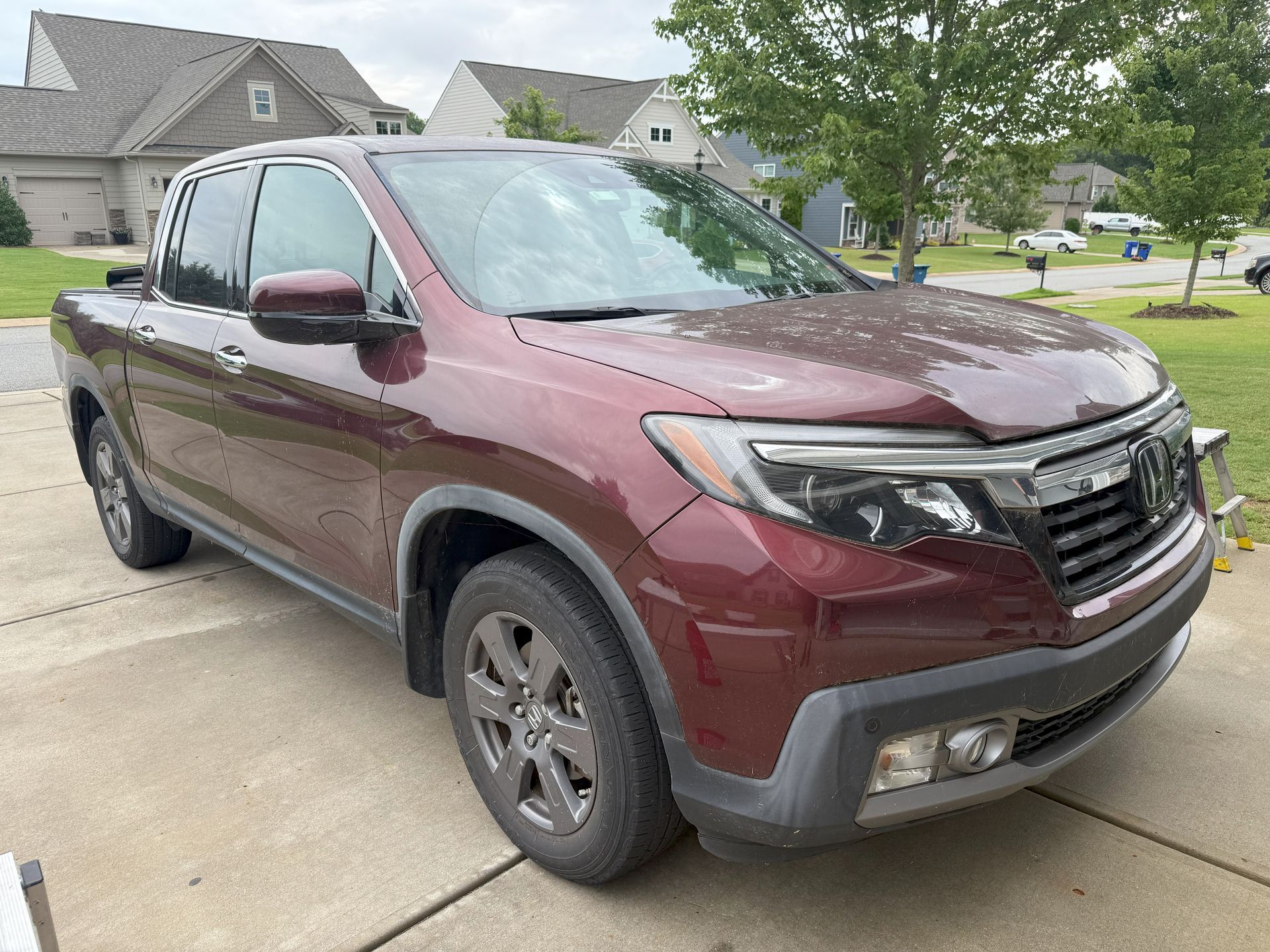 Burgundy Honda Ridgeline pickup truck parked on a driveway in front of a house.