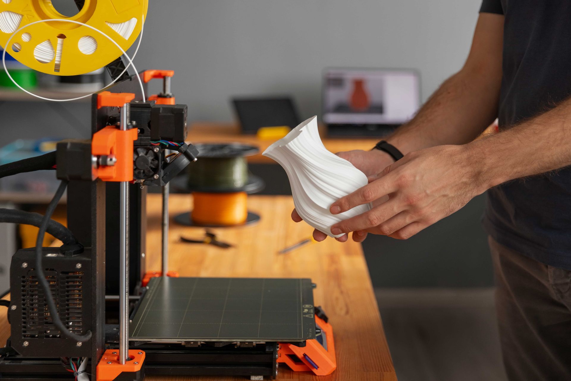 A man is holding a white object in front of a 3d printer.