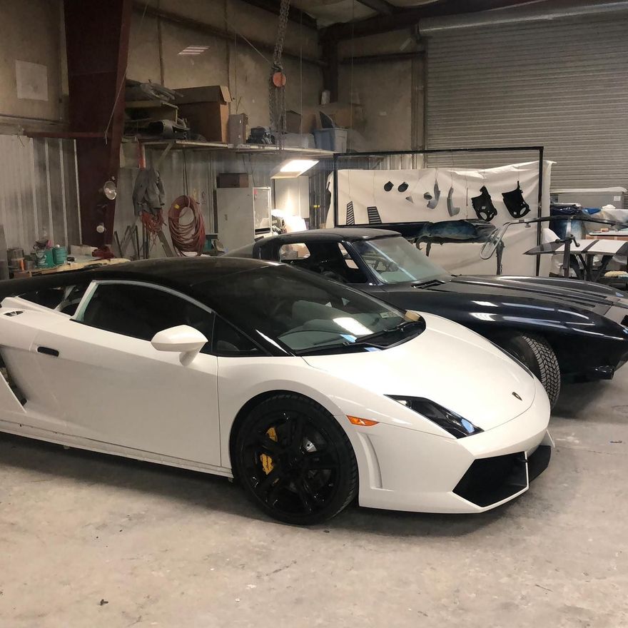 White Lamborghini and blue Corvette in a garage, next to equipment.