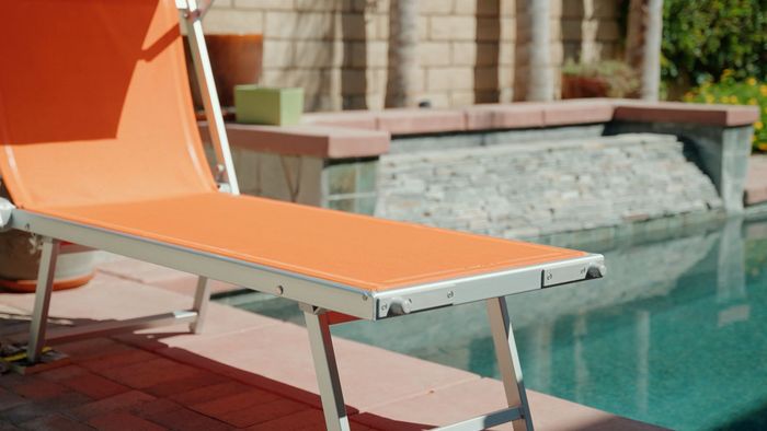 an orange lounge chair is sitting next to a swimming pool .