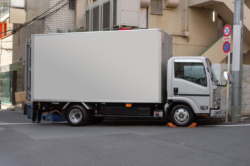 Silver Delivery Truck Parked on a City Street Near a Building and a Sign — Hines Logistic Pty Ltd In Maitland, NSW