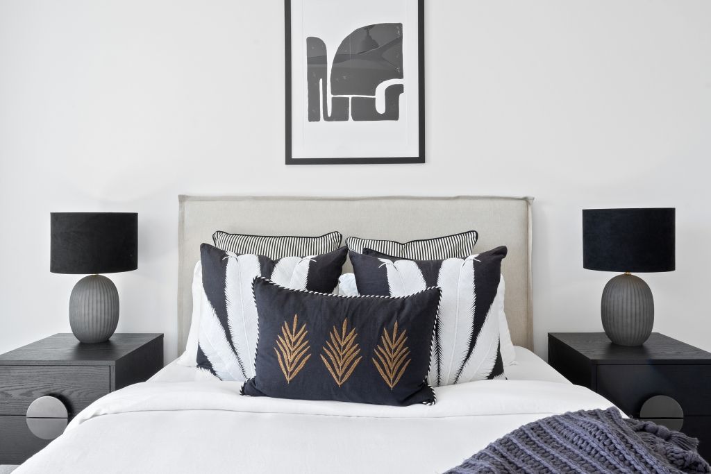 A bedroom with a bed , two nightstands , two lamps and a picture on the wall above the bed.