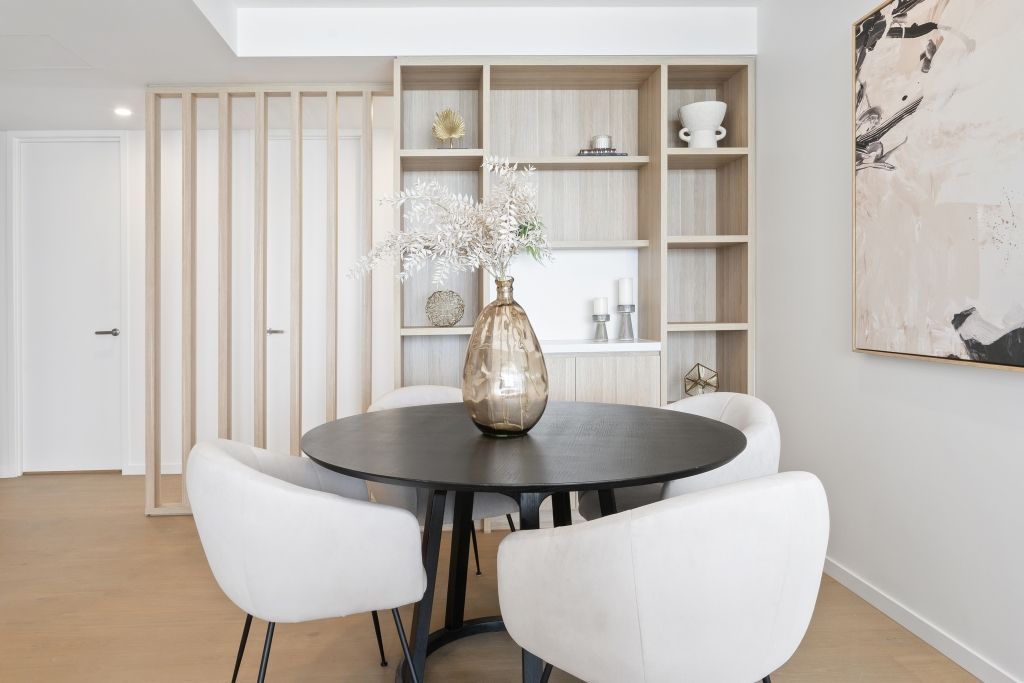 A dining room with a table and chairs and a vase of flowers on the table.
