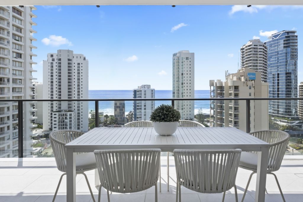 A balcony with a table and chairs overlooking the ocean and buildings.