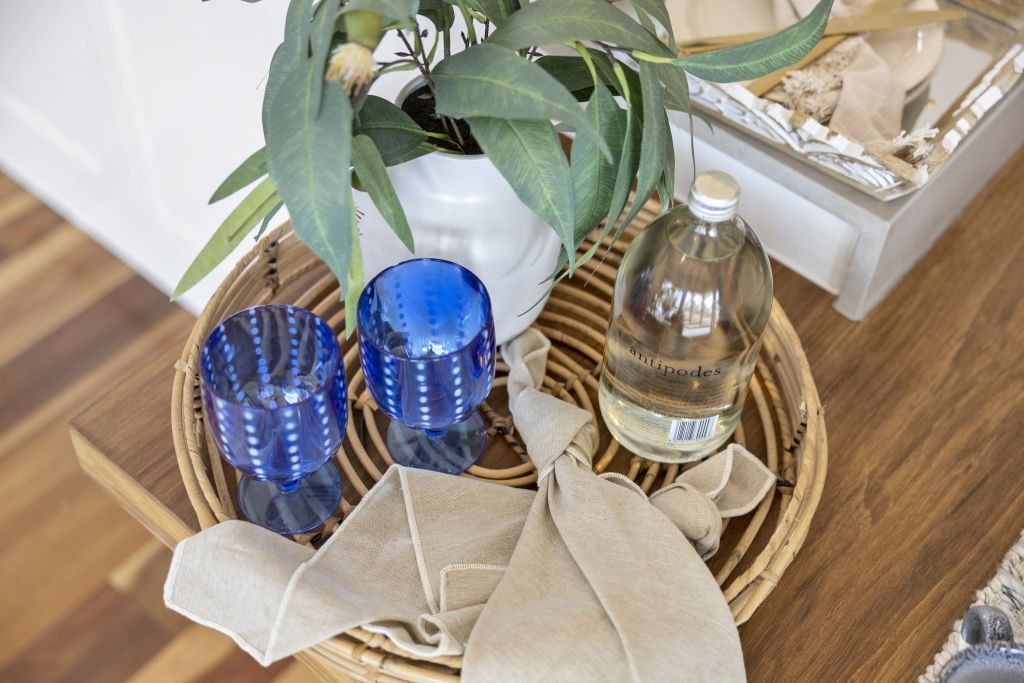 A wicker basket filled with glasses , napkins , a plant and a bottle of water.