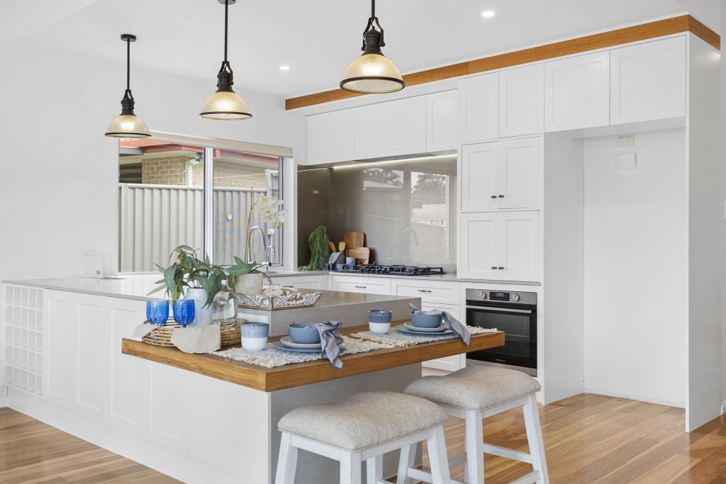 A kitchen with white cabinets , wooden floors , a table and stools.