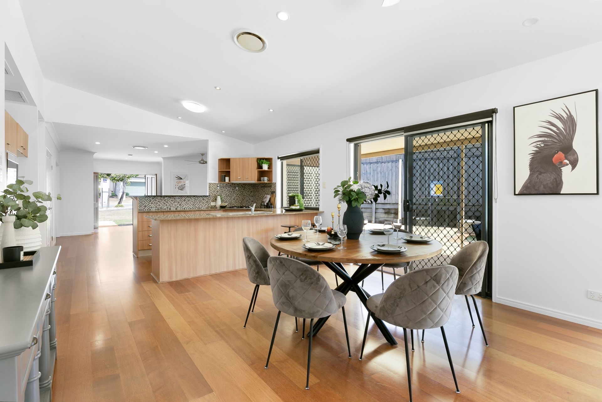 A dining room with a table and chairs and a picture of a cockatoo on the wall.