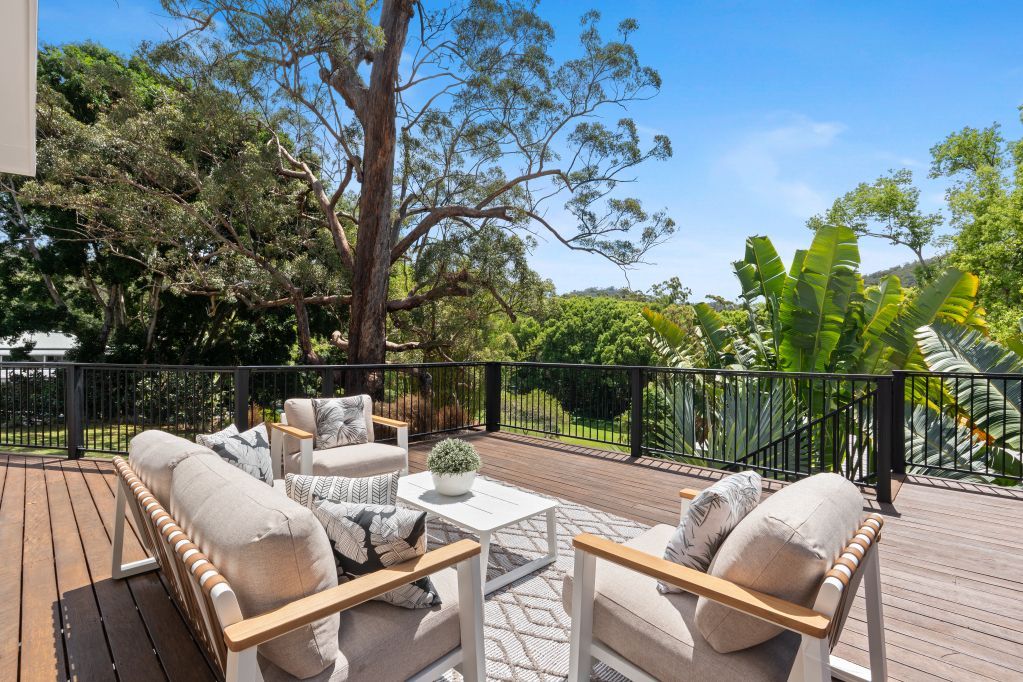 Patio seating area with cushioned chairs and table overlooking trees and a sunny garden.