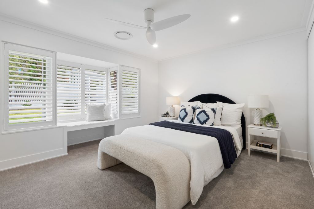 Bright white bedroom with a bed, window seat, and ceiling fan in neutral tones