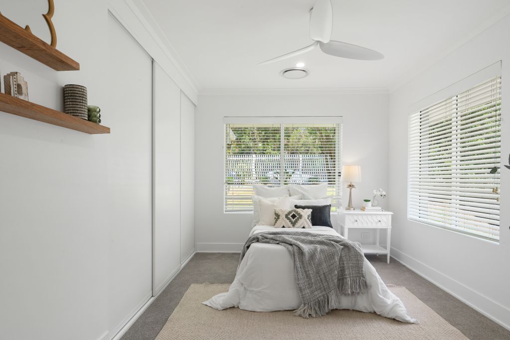 Bright minimalist bedroom with a bed, white walls, large windows, and a small desk.