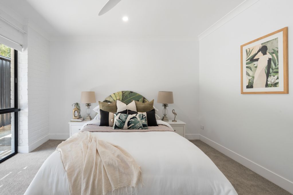 Bright bedroom with white bedding, twin lamps, and a framed wall print beside a window.