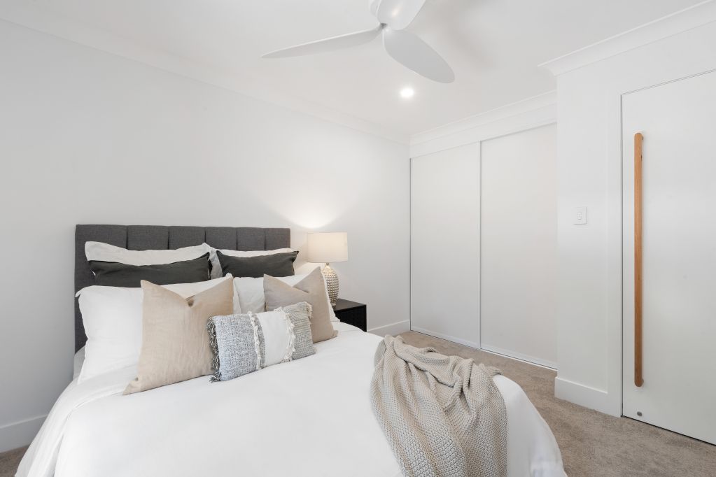 Bright minimalist bedroom with a white bed, beige pillows, and sliding closet doors