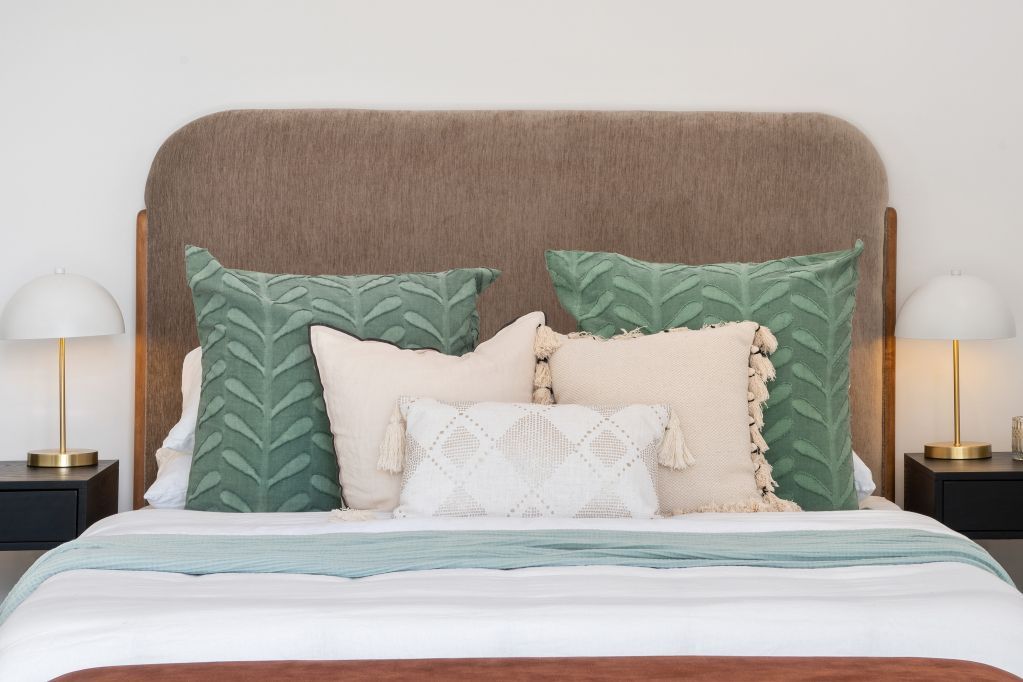 Cozy bed with beige headboard, green pillows, and matching bedside lamps in a neutral bedroom