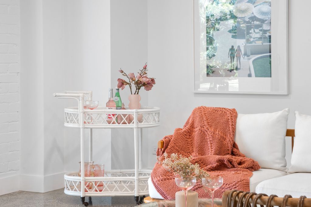 Bright white living room with coral throw on a sofa, floral cart, and framed art on the wall