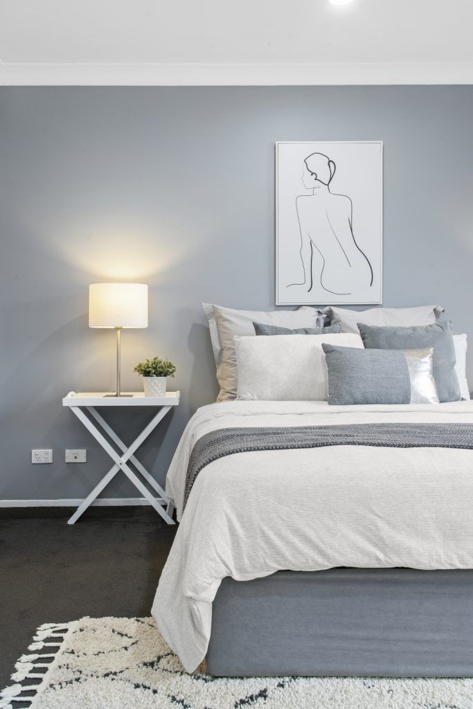 A bedroom with a bed , nightstand , lamp and painting on the wall.