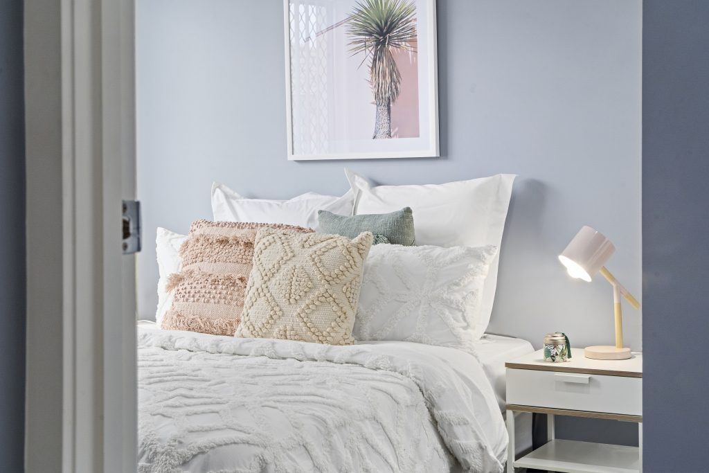 A bedroom with a bed , nightstand , lamp and a picture on the wall.