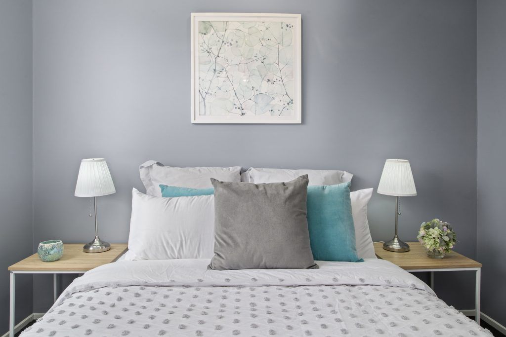 A bedroom with a bed , two nightstands , two lamps and a painting on the wall above the bed.