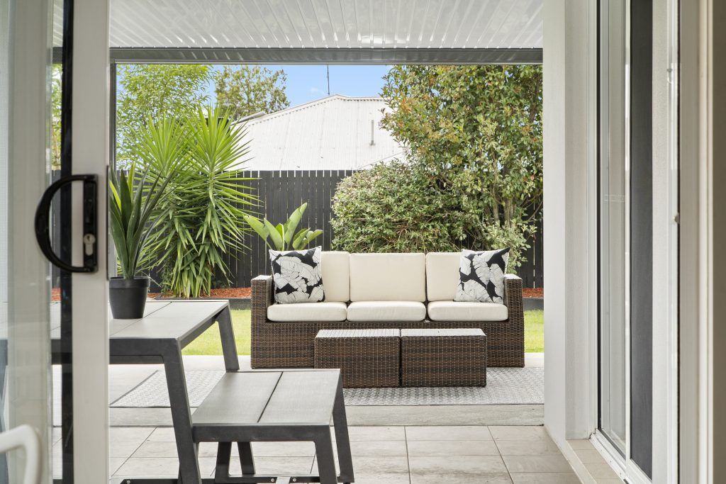 A patio with a couch , table , chairs and potted plants.