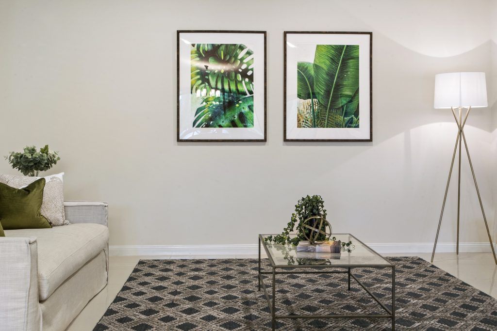 A living room with a couch , coffee table , rug and two paintings on the wall.