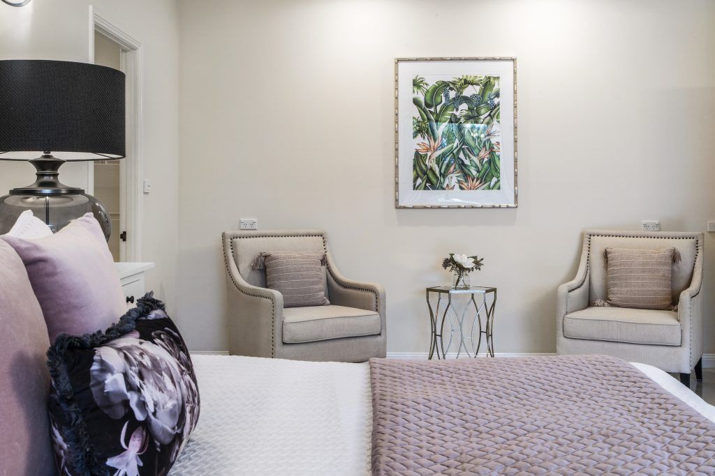 A bedroom with a bed , chairs , a lamp and a picture on the wall.