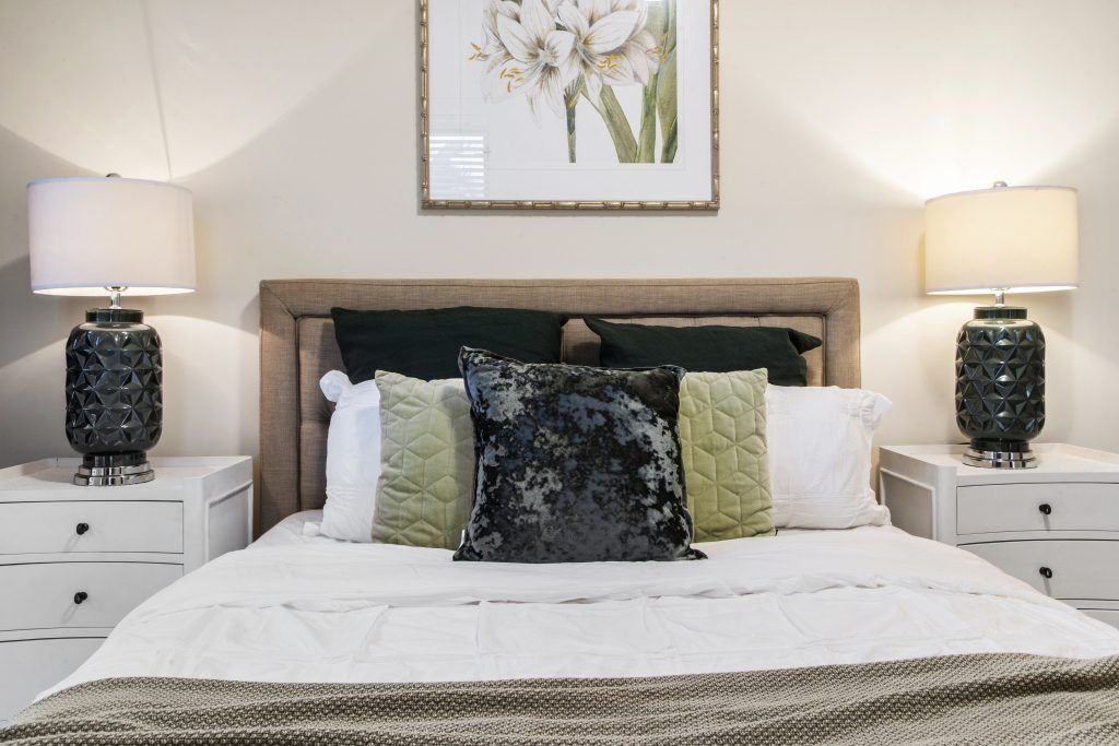 A bedroom with a bed , nightstands , lamps and a picture on the wall above the bed.
