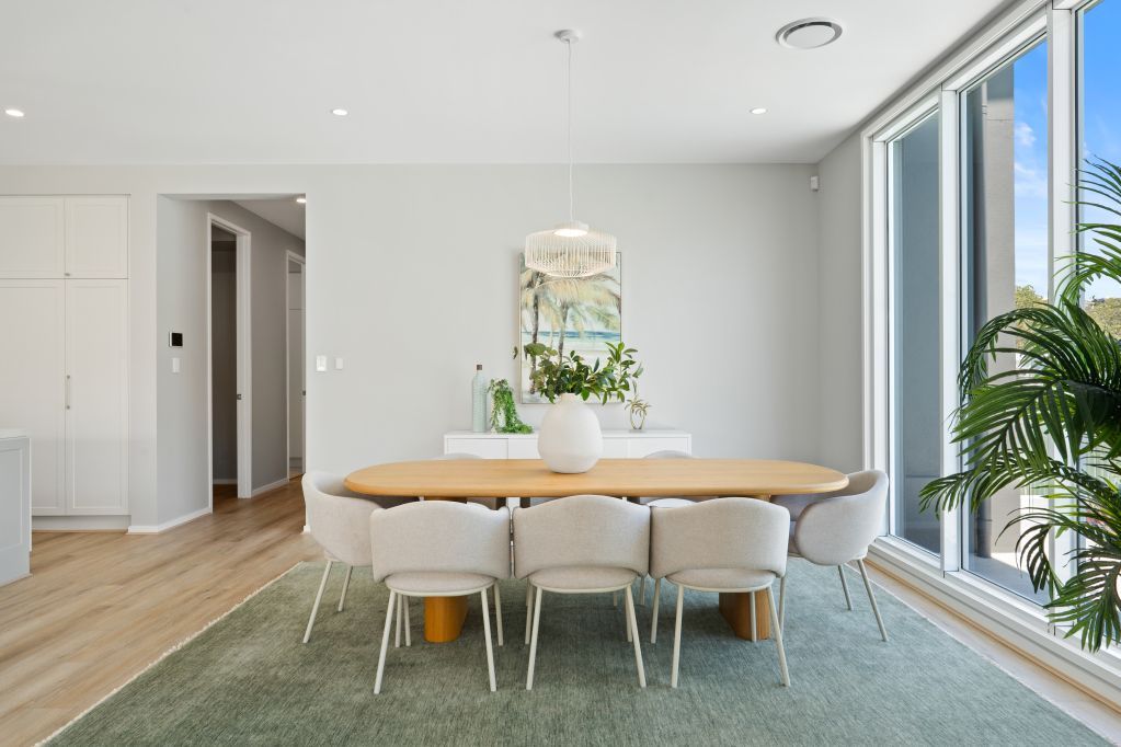 Bright dining room with oval table, white chairs, large windows, and green rug.