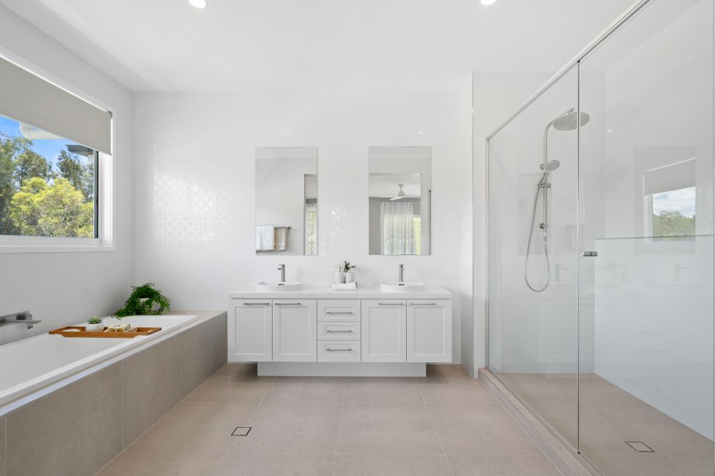 Bright modern bathroom with double vanity, glass shower, and large window letting in daylight