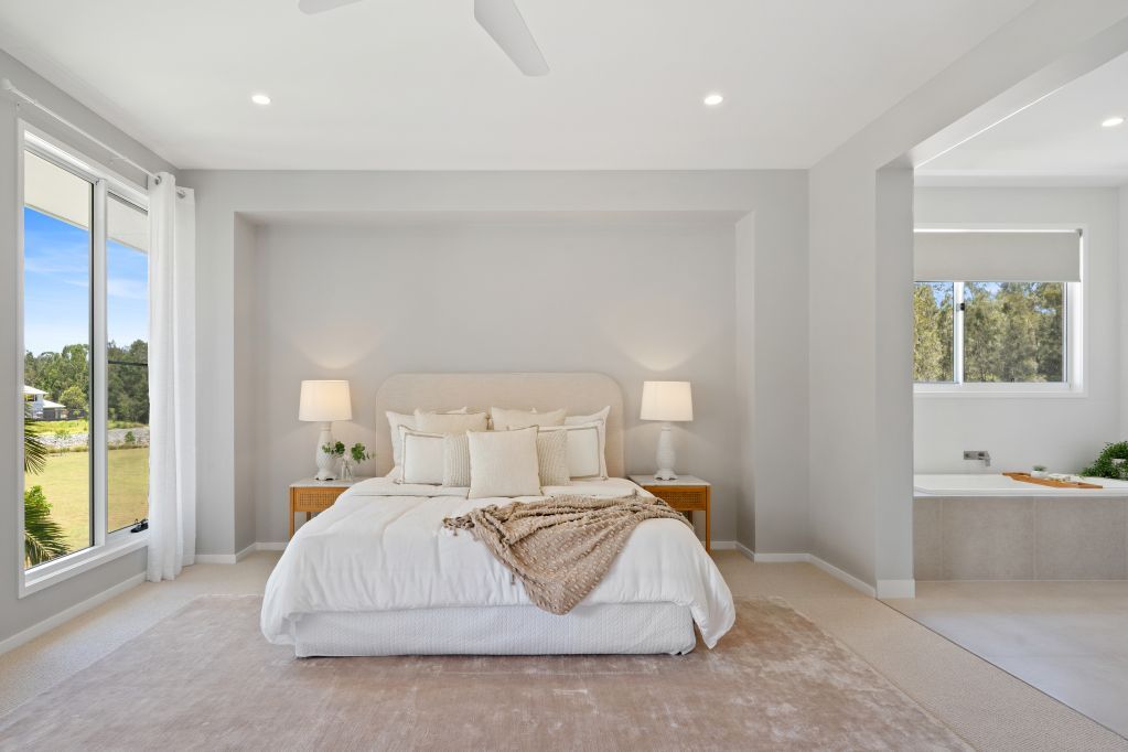 Bright minimalist bedroom with a white bed, nightstands, and large windows overlooking a green view