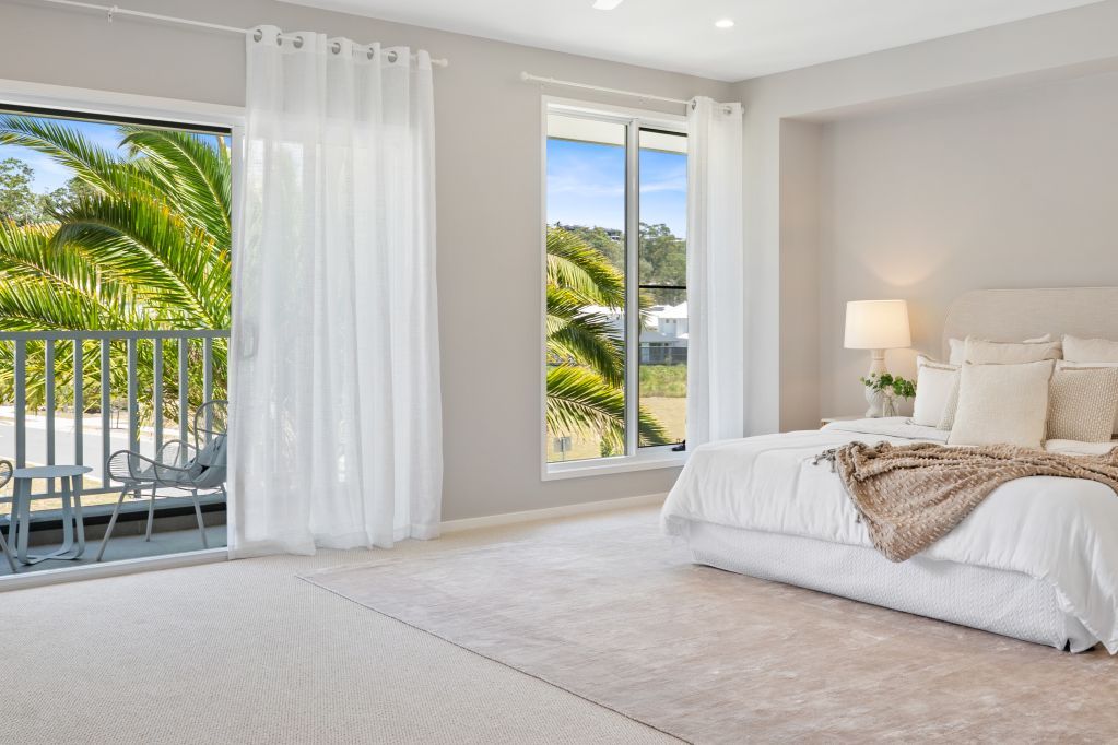 Bright bedroom with white bed, lamp, balcony doors, and palm trees outside.