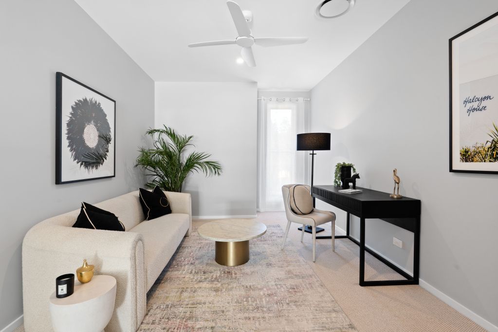 Bright minimalist living room with beige sofa, black desk, patterned rug, and large window.
