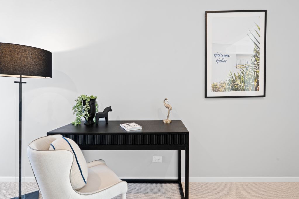 Minimalist corner with black desk, white chair, floor lamp, and framed wall art.