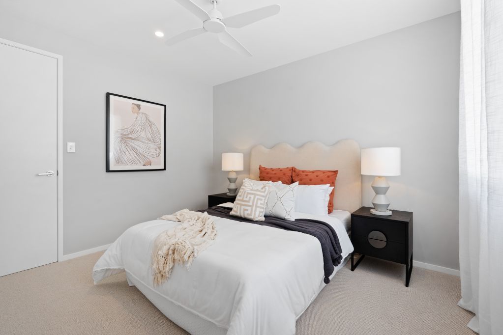 Bright bedroom with white bedding, black nightstands, and gray walls with framed art.