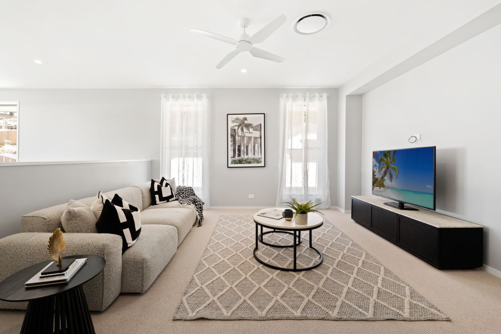 Modern living room with a gray sofa, patterned rug, wall-mounted TV, and coffee table by bright windows