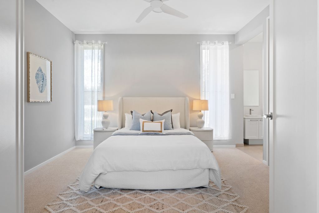 Bright, airy bedroom with a white bed, bedside lamps, tall windows, and soft gray decor