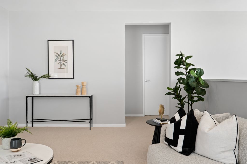 Minimalist living room with console table, wall art, plants, and a light sofa with black-and-white pillows