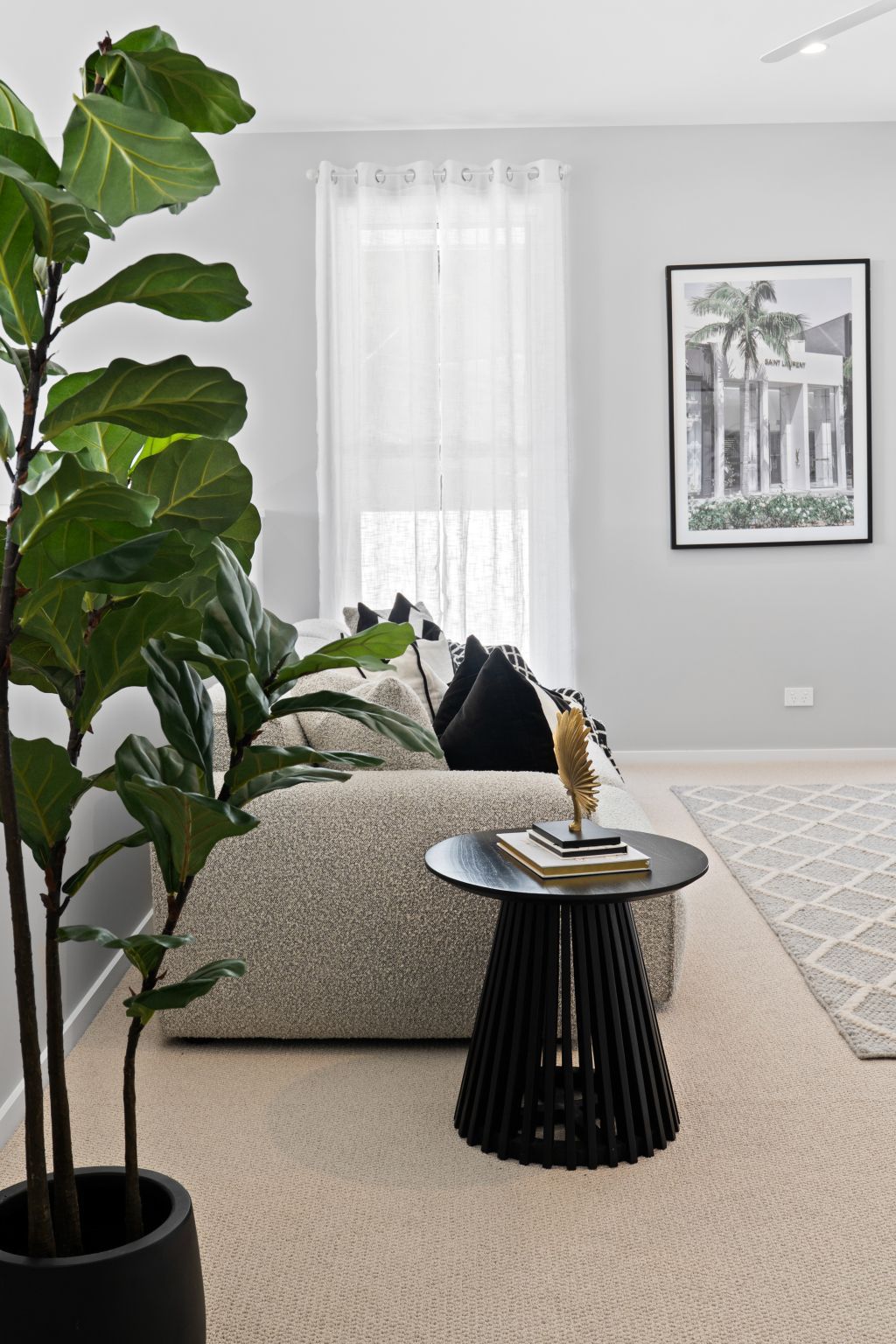 Bright living room with a large leafy plant, gray sofa, black side table, and framed wall art.