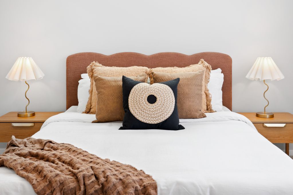Cozy bed with white linens, tan pillows, brown headboard, and matching bedside lamps in a minimalist bedroom