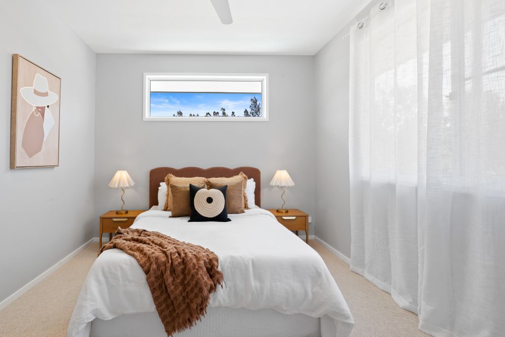 Bright, minimalist bedroom with a neatly made bed, warm accents, and large sheer-curtained window