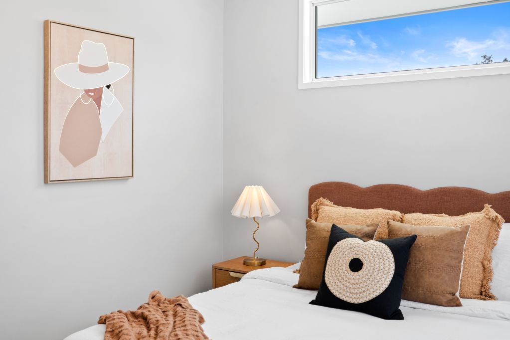 Cozy bedroom with tan headboard, white bedding, bedside lamp, and framed wall art.