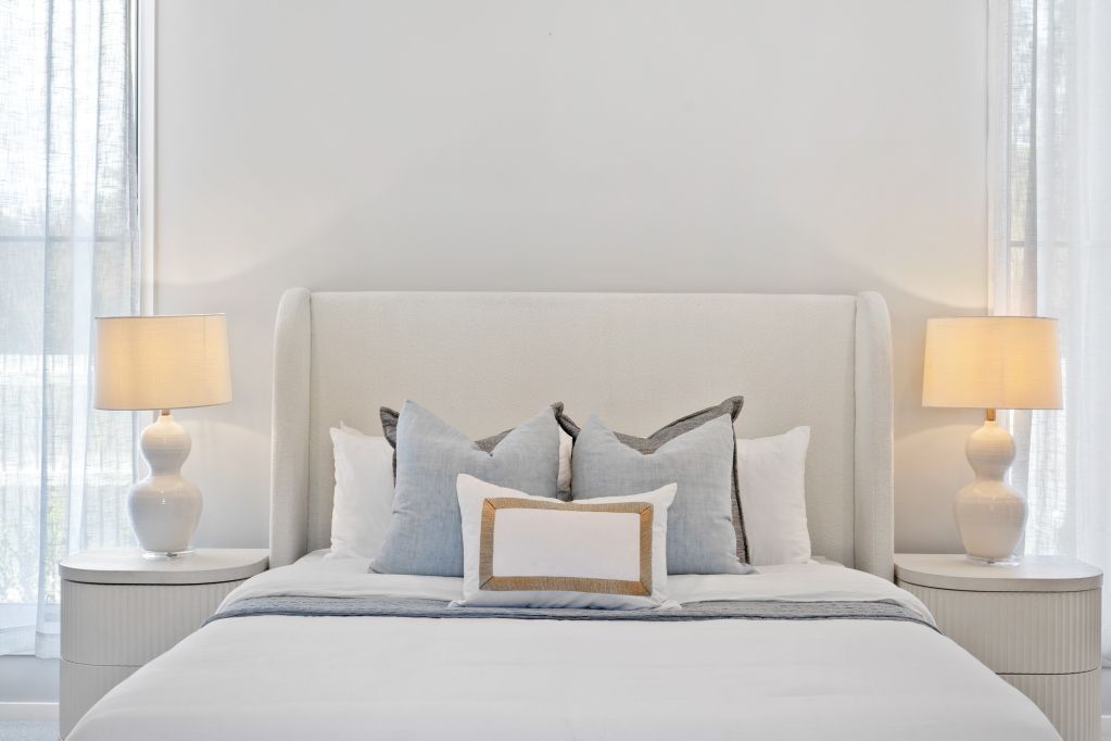 Bright bedroom with a white bed, gray pillows, and matching bedside lamps by sheer curtains