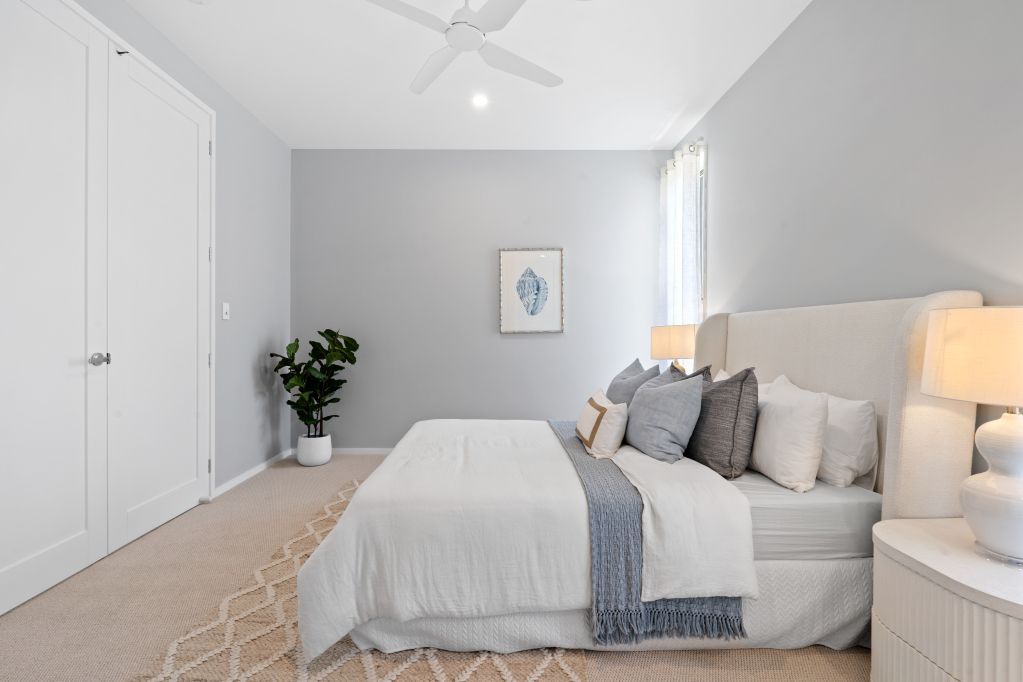 Bright white bedroom with a bed, nightstand, plant, and closet near a window.