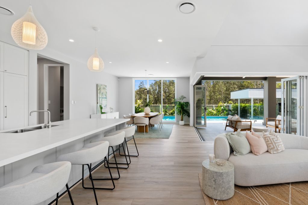 Bright modern open-plan living room with white bar seating, sofa, and large sliding glass doors to greenery