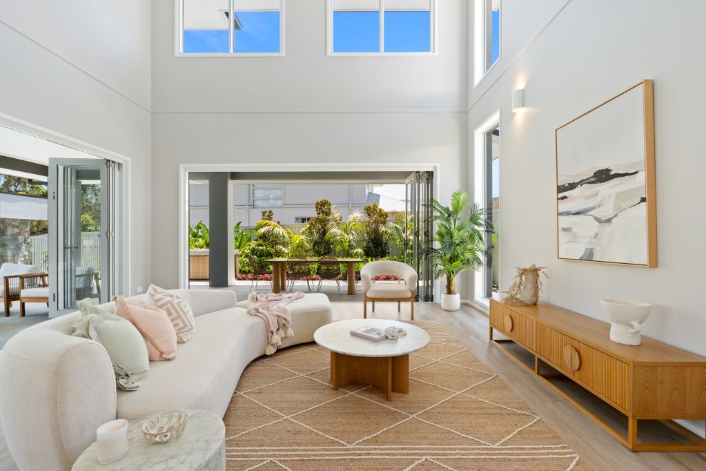 Bright modern living room with white sofa, round coffee table, large windows, and wooden console table