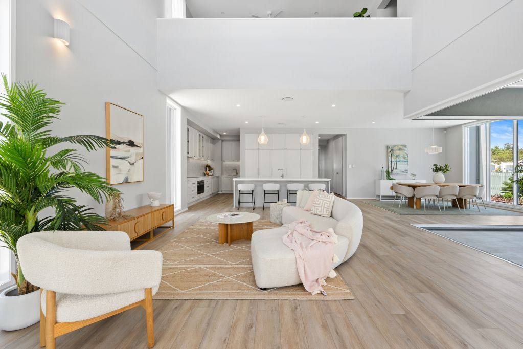 Bright modern living room with white sofas, wood floors, and large windows overlooking water