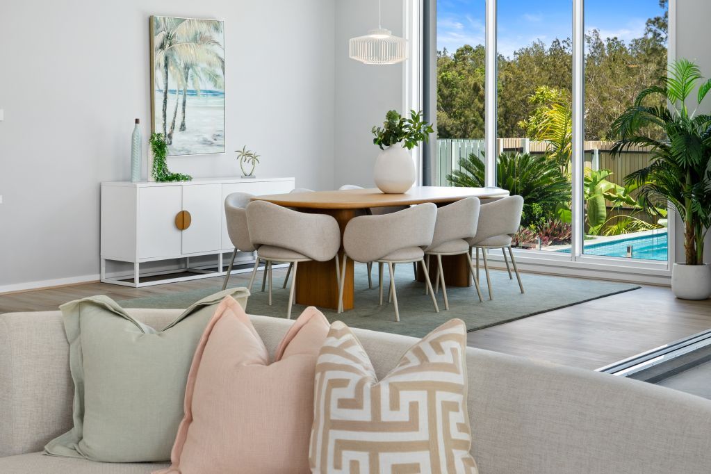 Bright modern dining room with beige chairs, light wood table, sofa pillows, and sliding doors to a pool.